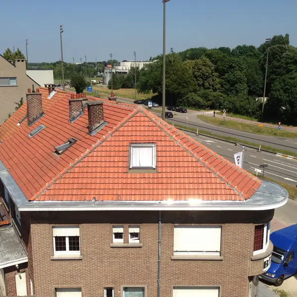 Toiture en tuiles rouges rénovée sur une maison d'angle, avec fenêtre de toit