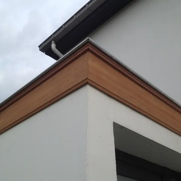 Habillage de corniche en bois sur une façade enduite blanche