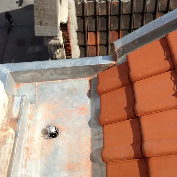 Chéneau en zinc avec avaloir au pied d'une toiture en tuiles