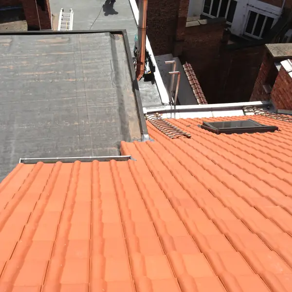 Toiture en tuiles rouges rénovée à côté d'une toiture plate