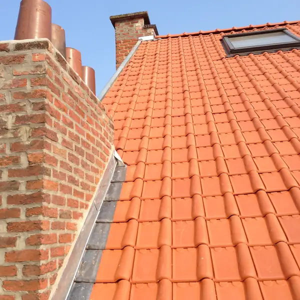 Solin en zinc le long d'une cheminée en briques sur une toiture en tuiles