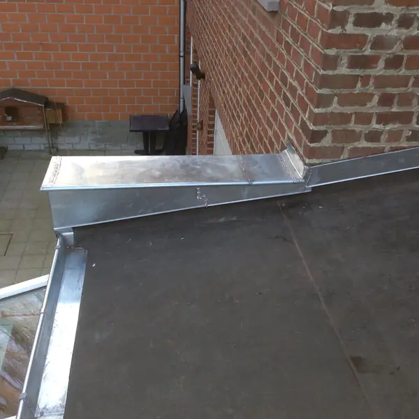 Relevé et solin en zinc sur une toiture plate contre un mur en briques
